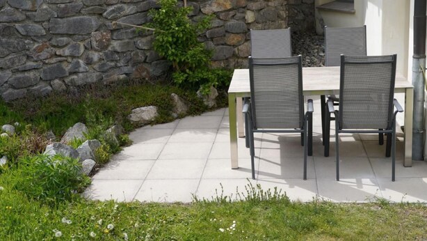 Eine Terrasse mit einer Steinsäule, zwei Stühlen und einem Tisch.
