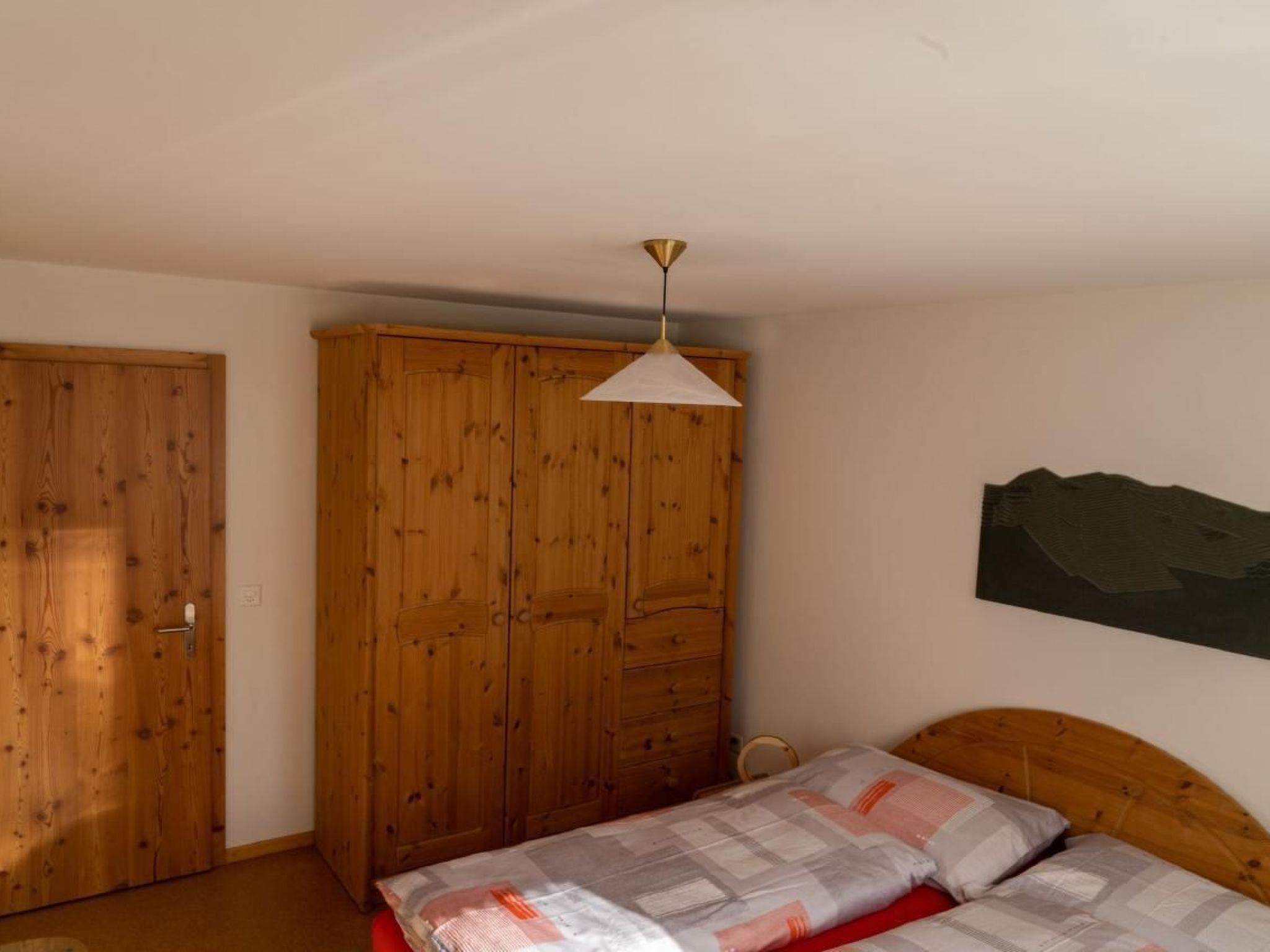 Una camera da letto con un'armadio in legno, un letto con testiera e una lampada a sospensione.
