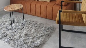 En moderne stue med en brun sofa, et rundt træbord, en blød grå måtte og en gul lænestol.