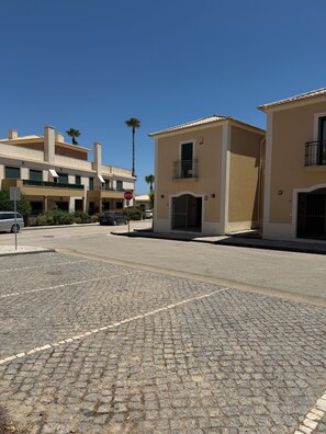 A residential street with a cobblestone sidewalk, a stop sign, and buildings with balconies and a gated entrance.