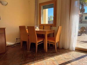 Ein Essbereich mit Holztisch und Stühlen, einem Fenster mit Vorhängen und Blick ins Freie.