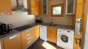 Ett kompakt kök med träskåp, en inbyggd diskmaskin, en tvättmaskin och ett fönster ovanför diskbänken.