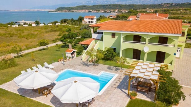 Una villa grande con piscina, mobiliario exterior y vistas al mar.