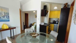 Un comedor moderno con una mesa de vidrio y cuatro sillas, una cocina con armarios amarillos y un cuadro en la pared.