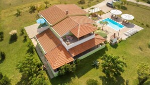 Una casa de dos pisos con piscina, mobiliario de exterior y jardín.