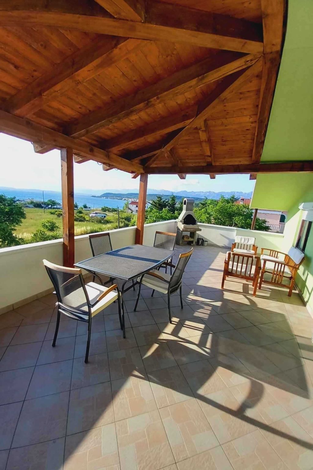 A covered patio with a table and chairs, a grill, and a view of the landscape.