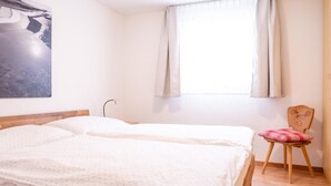 A bedroom with a bed, a chair, a window with curtains, and a wall-mounted lamp. - Chesa La Capriola by Interhome (Sils Maria)