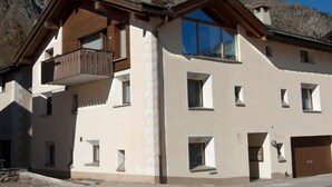 A two-story building with a balcony on the upper floor, a garage door on the right, and a clear view of the surrounding mountains. - Chesa La Capriola by Interhome (Sils Maria)