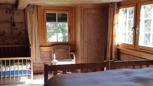 A wooden cabin room with a bed, a window, a chair, and a view of trees. - Rietberg 8 Braunwald by Interhome (Braunwald)