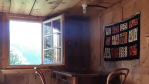 A wooden cabin room with a large window, a wooden table, two chairs, and a wall hanging. - Rietberg 8 Braunwald by Interhome (Braunwald)