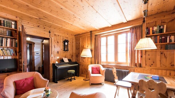 L’intérieur d’un chalet en bois chaleureux et accueillant, avec un piano, des étagères à livres, une table à manger et des sièges confortables.