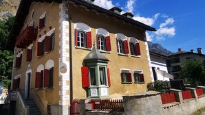 Un bâtiment traditionnel doté d’un toit à forte pente, de volets rouges et d’une tour centrale avec une porte verte.