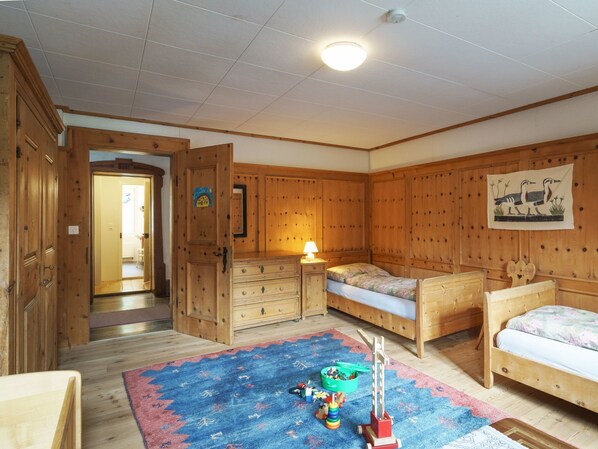 A room with wooden walls and floors, two wooden beds, a dresser, a lamp, and a colorful rug.
