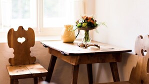 Une table en bois sur laquelle se trouve un vase de fleurs, une carafe en céramique et une chaise en bois avec une découpe en forme de cœur.