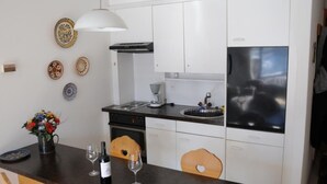 Una cucina moderna con mobili bianchi, un frigorifero nero, una macchina per il caffè e un'area pranzo con tavolo e sedie in legno.