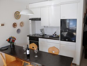Eine moderne Küche mit weißen Schränken, einem schwarzen Kühlschrank, einer Kaffeemaschine und einem Essbereich mit Holztisch und Stühlen.
