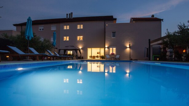 A swimming pool with lounge chairs and umbrellas, a building with multiple windows, and outdoor lighting. - Ferienvilla , Schwimmbad, Imotski, Makarska by Interhome (Donji Vinjani)