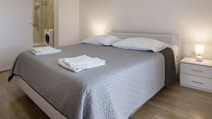 A neatly made bed with a grey quilt, two white pillows, and folded white towels on the side. There is a bedside table with a lamp and a small drawer. - Ferienvilla , Schwimmbad, Imotski, Makarska by Interhome (Donji Vinjani)