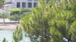 Un bâtiment situé sur la côte, doté d’un toit recouvert de tuiles, entouré de verdure et bordé par une étendue d’eau.