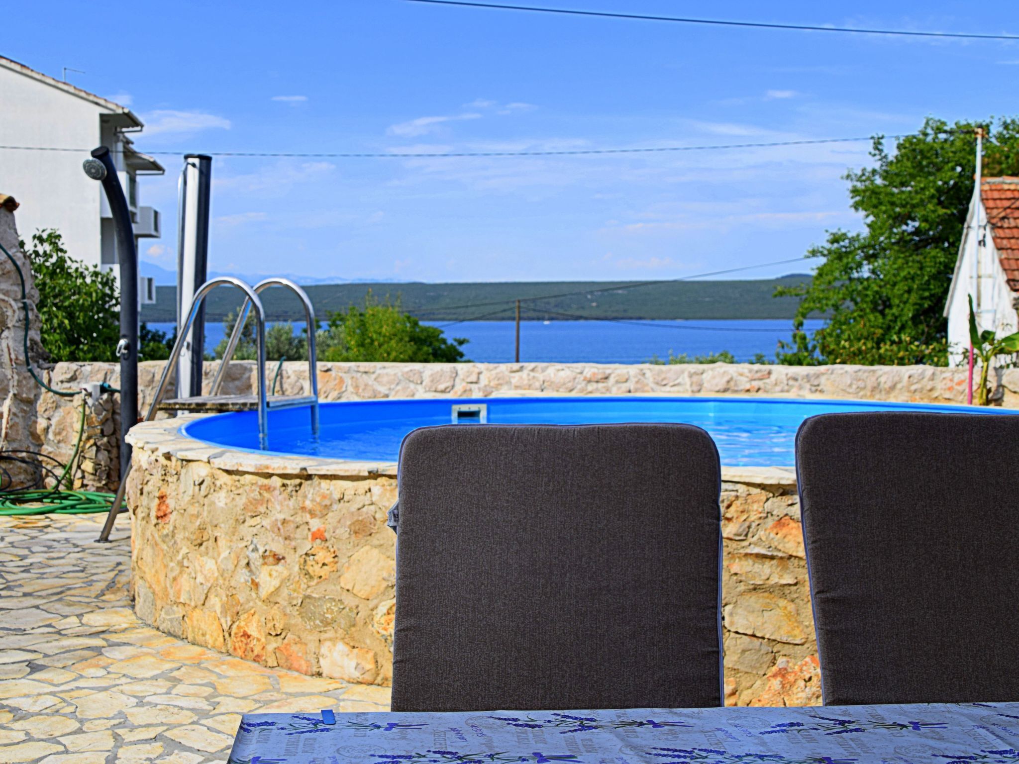 Une piscine en pierre, avec deux chaises, une table et une vue sur la mer.