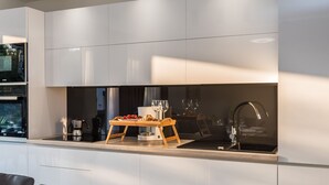 A modern kitchen with white cabinetry, a built-in oven, a coffee maker, and a wooden serving tray with food and wine glasses. - Villa Rossa by Interhome (Ugljan/Kukljica)