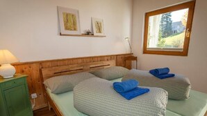 Une chambre avec deux lits, une table de chevet verte, une tête de lit en bois et une fenêtre donnant sur des arbres.