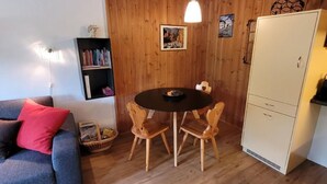 Une pièce chaleureuse avec un mur en bois, une table ronde entourée de chaises, une bibliothèque et une armoire.