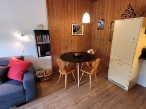 A cozy room with a wooden wall, a round table with chairs, a bookshelf, and a wardrobe. - Yvonne Mayer by Interhome (Scuol)