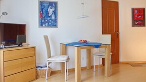 Una stanza con un armadio in legno, una televisione, un tavolo da pranzo con sedie e due quadri appesi alle pareti.