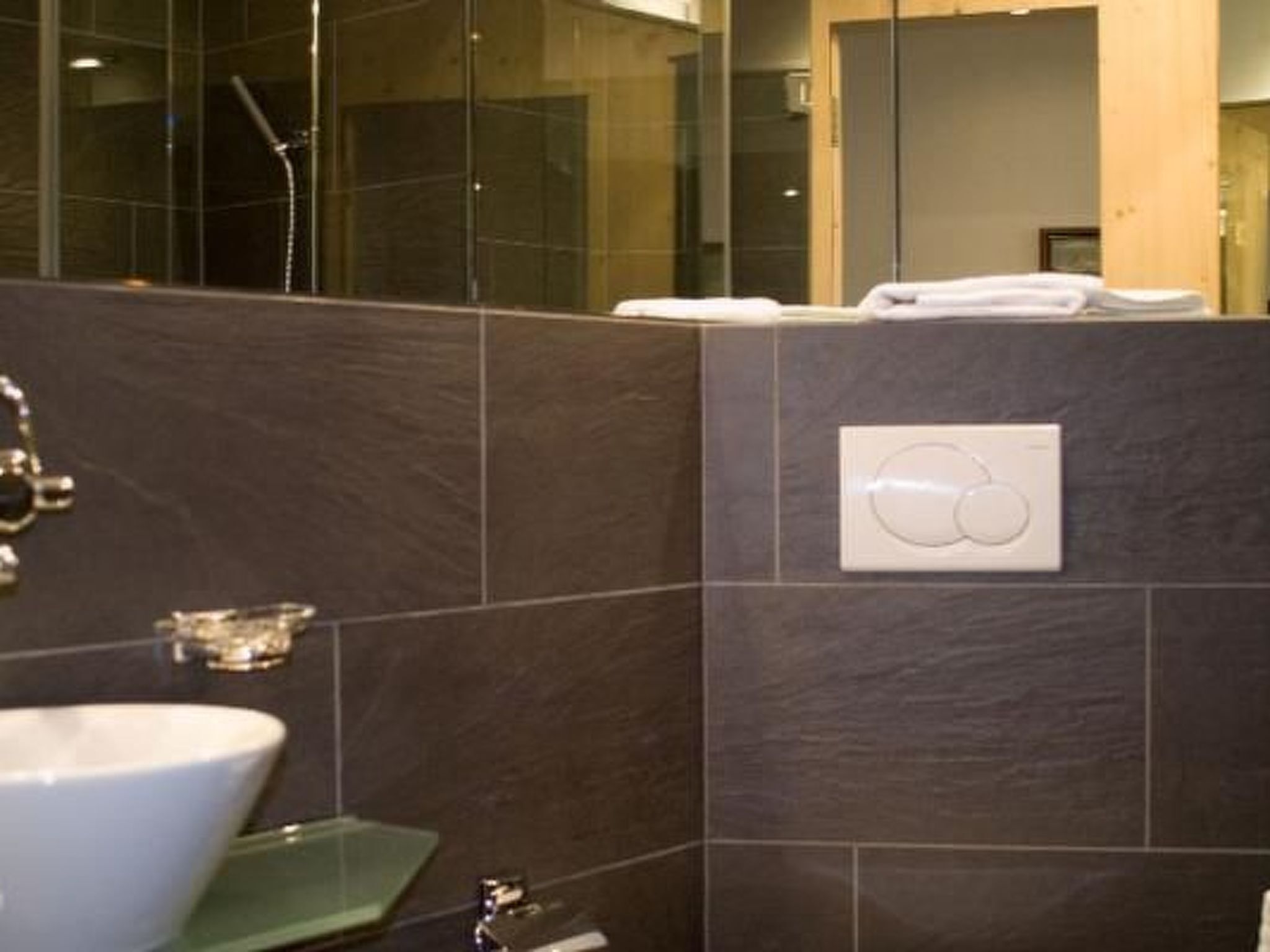A modern bathroom with a large white sink, a glass shower enclosure, and a towel rack with folded towels.