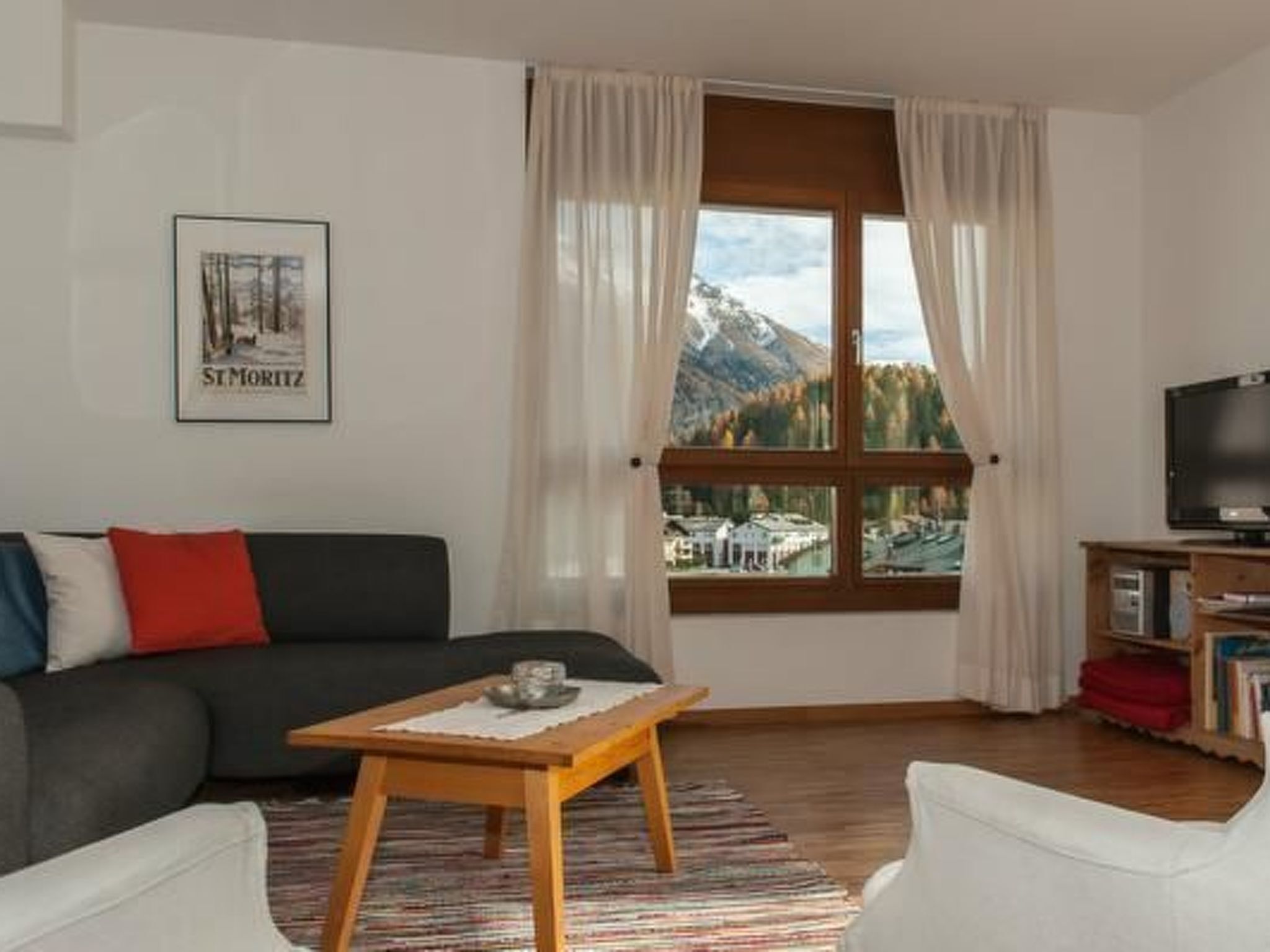 A living room with a sofa, a coffee table, a TV, and a window with a mountain view.