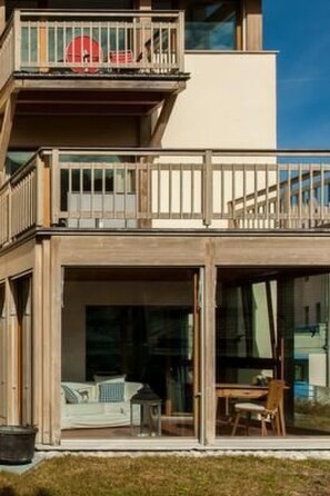 Un bâtiment moderne à deux étages, doté d’un balcon et de grandes portes vitrées donnant sur un espace intérieur.