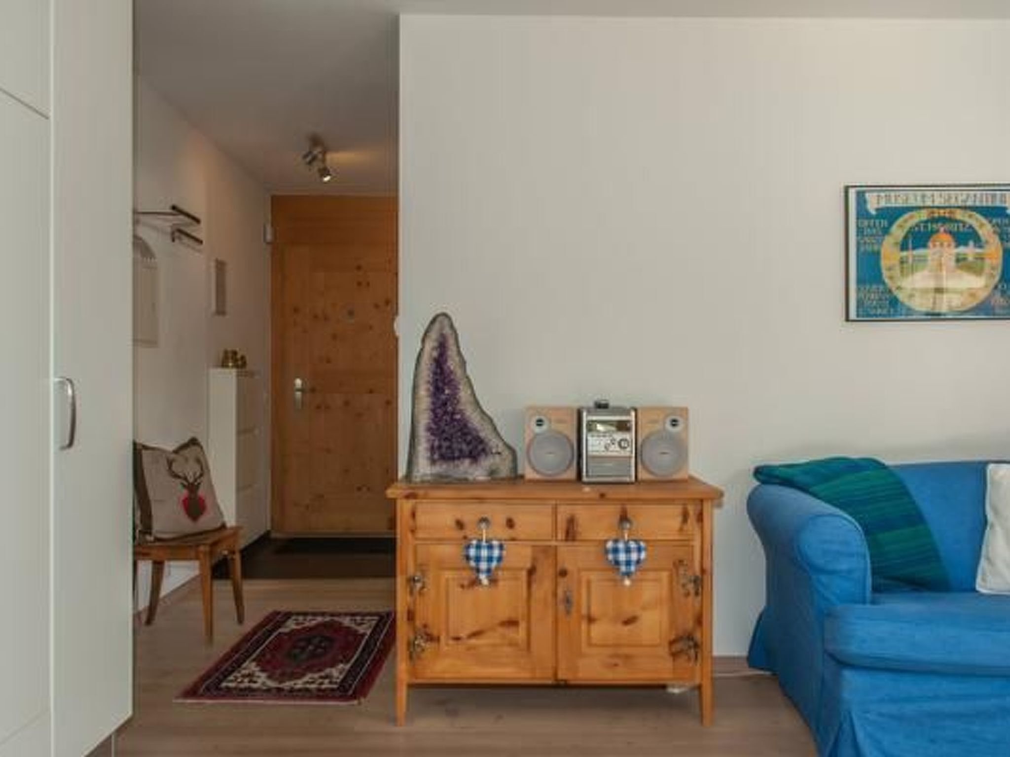 A room with a blue sofa, wooden cabinet with checkered cloths, a radio, and a poster on the wall.