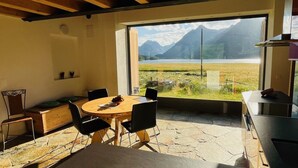 Ein Essbereich mit Holztisch und Stühlen, Blick auf Berge und See durch große Fenster.