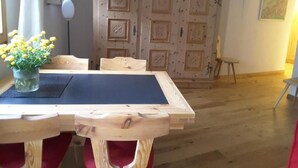 Un comedor con una mesa y sillas de madera, un florero con flores amarillas y una puerta de madera decorativa al fondo.