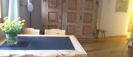 Ein Essbereich mit Holztisch und -stühlen, einer Vase mit gelben Blumen und einer dekorativen Holztür im Hintergrund.