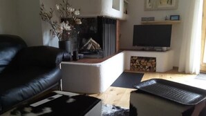 Una sala de estar con un sofá de cuero negro, un reposapiés blanco, un reposapiés estampado en blanco y negro, una chimenea, un televisor y un cuadro en la pared.