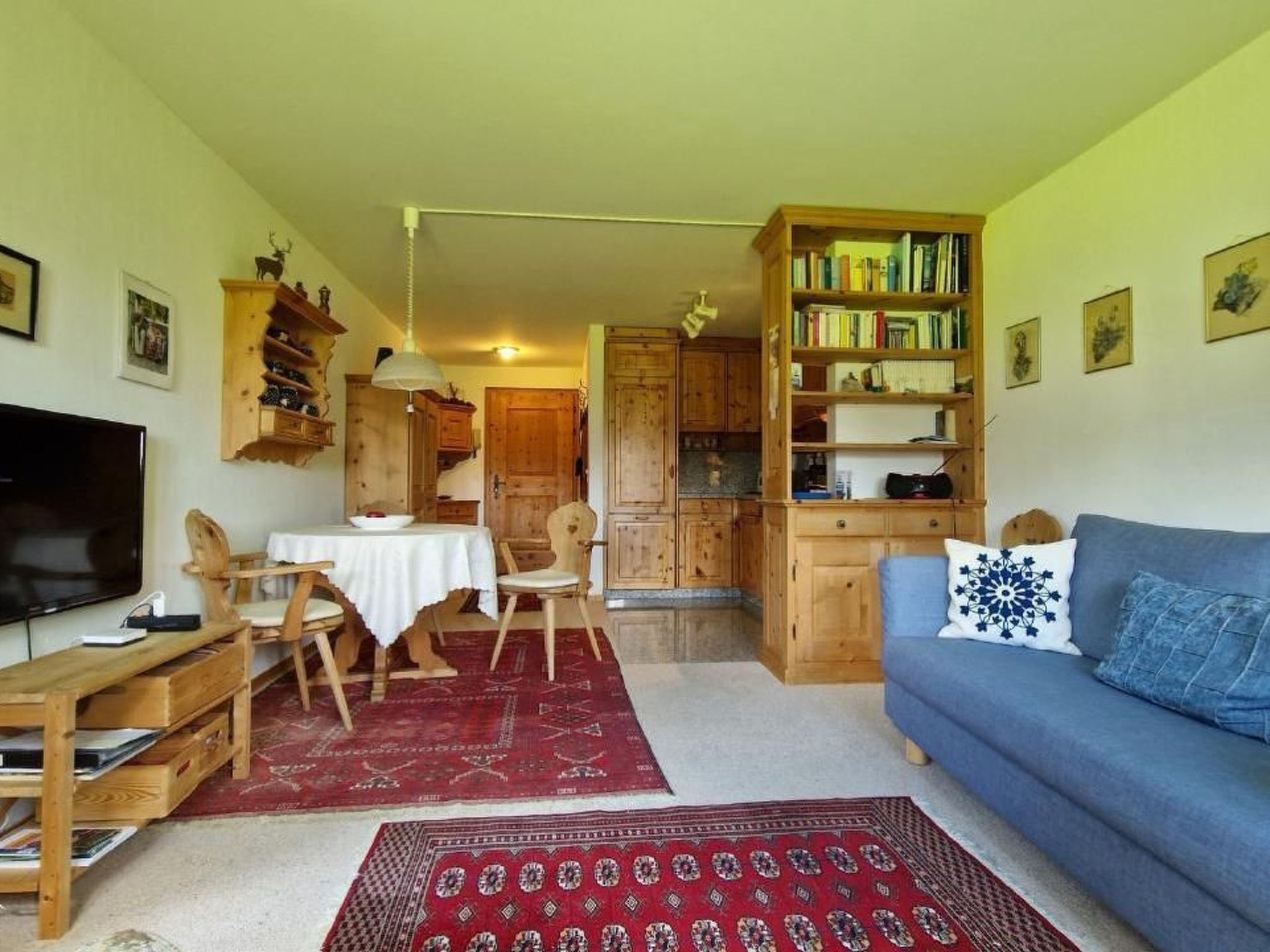 Un accogliente soggiorno con un divano blu, mobili in legno, un televisore e una libreria.