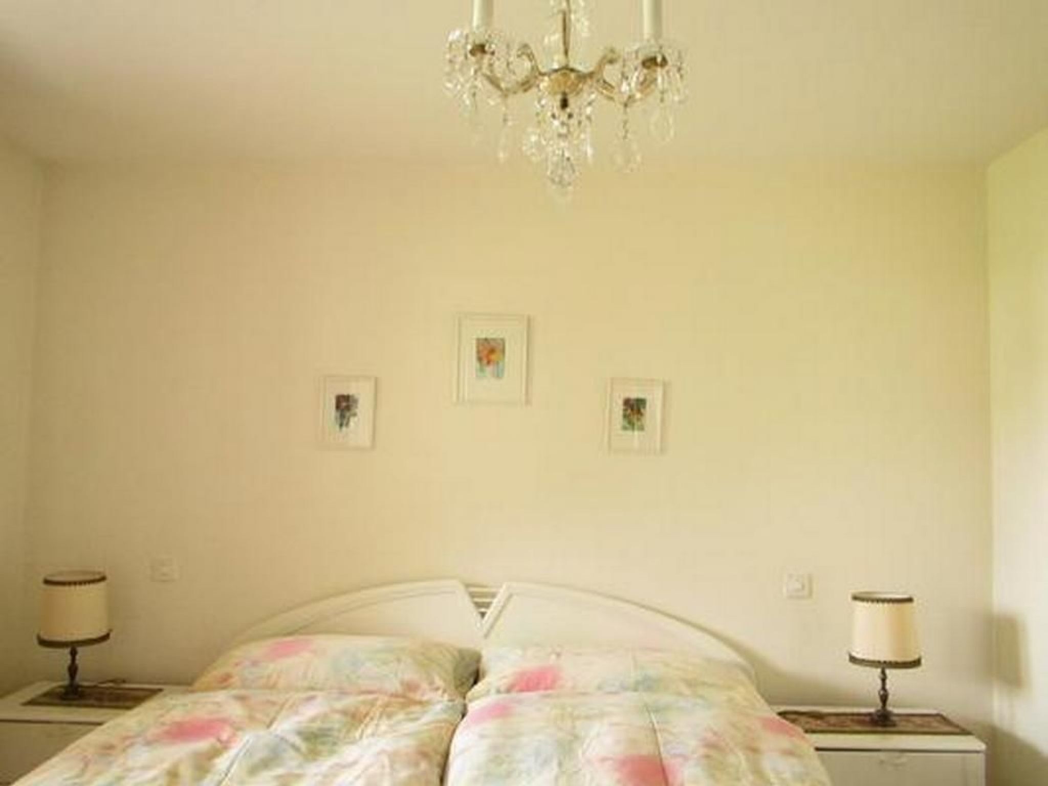 Une chambre à coucher avec un lit, deux tables de chevet, un lustre et trois tableaux encadrés accrochés au mur.