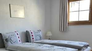 Ein Schlafzimmer mit zwei Einzelbetten, einem Fenster mit Vorhängen, einer Nachttischlampe und einem gerahmten Bild an der Wand.