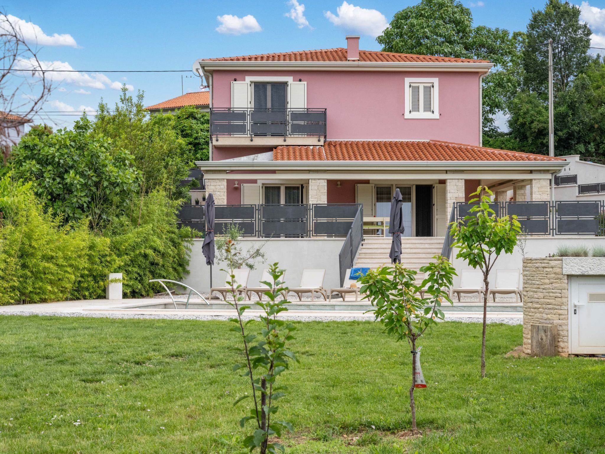 A two-story house with a balcony, a small garden, and a paved driveway.