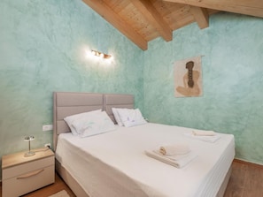 Un dormitorio con cama, mesita de noche, lámpara de pared e imagen enmarcada.