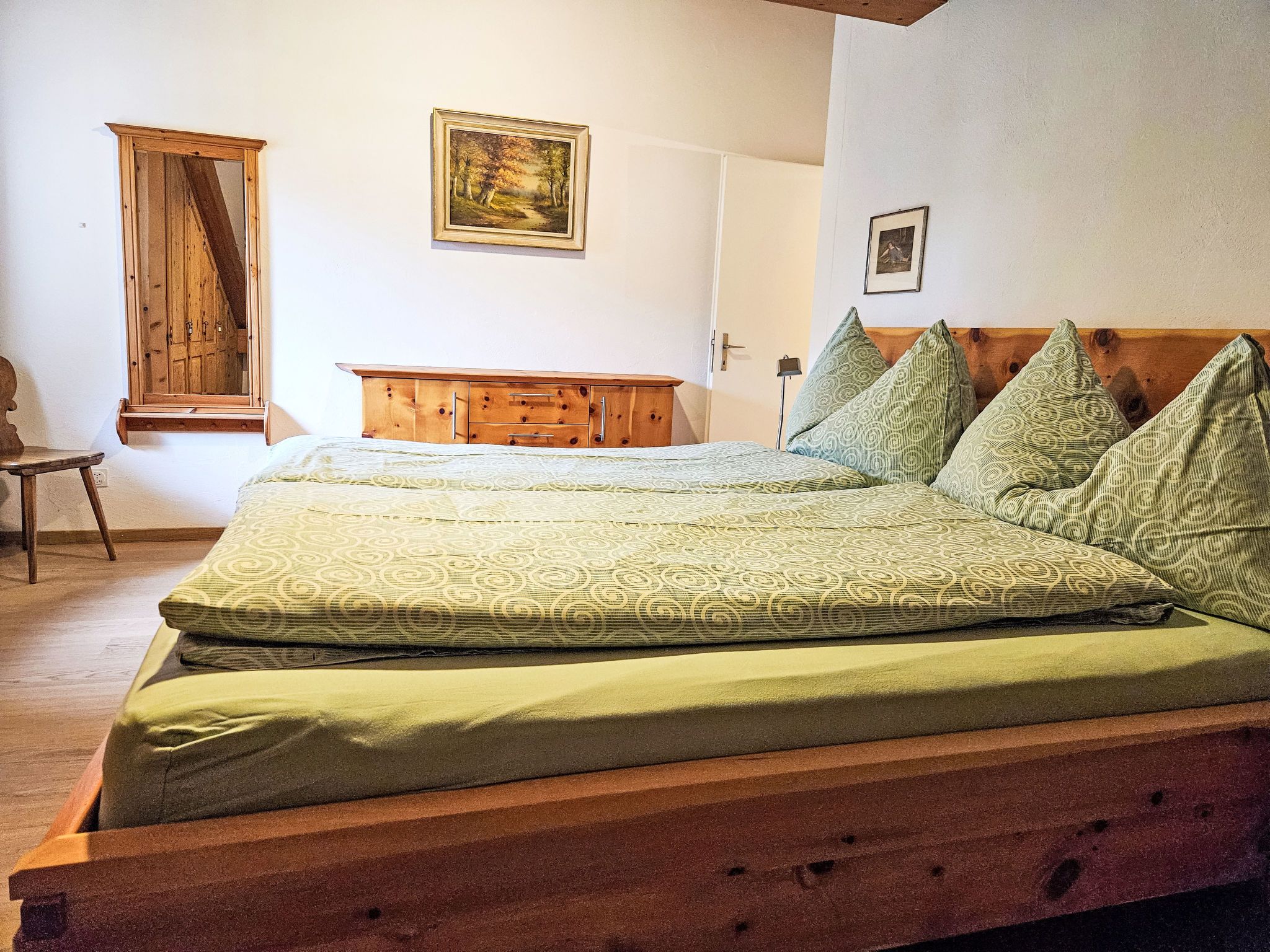 Un dormitorio con una cama y cómoda de madera, una silla y dos cuadros en la pared.