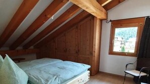 A small attic bedroom with a wooden ceiling, a single bed, a desk, and a window with a view of the outside. - Chesa Foppas Nr. 7 by Interhome (Sils Maria)