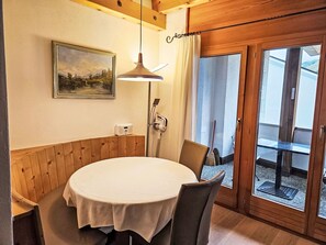 A dining area with a round table, chairs, a painting, a lamp, and a sliding glass door leading outside. - Chesa Foppas Nr. 7 by Interhome (Sils Maria)
