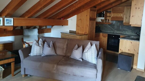 A cozy living room with a sofa, wooden beams, a kitchen area, and a dining table. - Chesa Foppas Nr. 7 by Interhome (Sils Maria)
