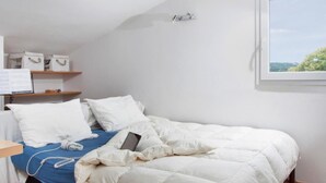 Une chambre à coucher comprenant un lit, une table de chevet, une étagère avec des boîtes de rangement, une fenêtre donnant sur un paysage agréable et un thermostat fixé au mur.