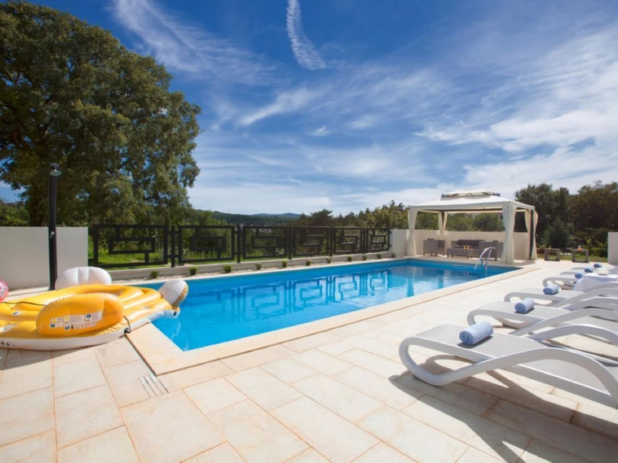 A swimming pool with lounge chairs and a covered seating area.