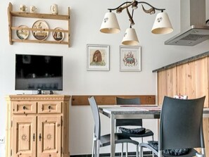 Ein Essbereich mit einem Holzschrank, einem Fernseher, einer Chandelierleuchtre und zwei gerahmten Bildern an der Wand.
