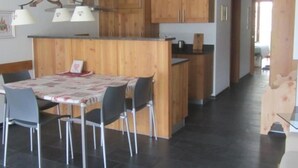 Uma cozinha moderna com armários de madeira, uma área de refeições com mesa e cadeiras, e um corredor que dá para outro cômodo.